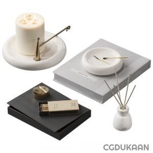 A still-life photo of various home decor items including a lit three-wick candle on a white dish with a brass wick dipper, a white ashtray with a single matchstick, a black rectangle serving tray with a brass match holder and matchsticks, a stack of grey books, and a white reed diffuser with multiple reed sticks on a white surface.