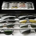 A display of various designer sunglasses on glass shelves with the text "BESPECTACLED model by Aviato" at the bottom.